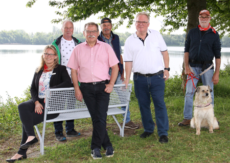 Kathrin Hüsch von der Sparkasse am Niederrhein, Wolfgang Clanzett vom Initiativkreis, Ortsvorsteher Edgar Giesen, Karl Heinz Ladwig und Franz-Josef Spölmink vom Heimat- und Verkehrsverein sowie Hans-Josef Angenendt (Initiativkreis) mit Bella an einer von insgesamt drei neuen Bänken, die Spaziergänger am Ufer des Menzelener Freizeitsees zum Verweilen einladen.